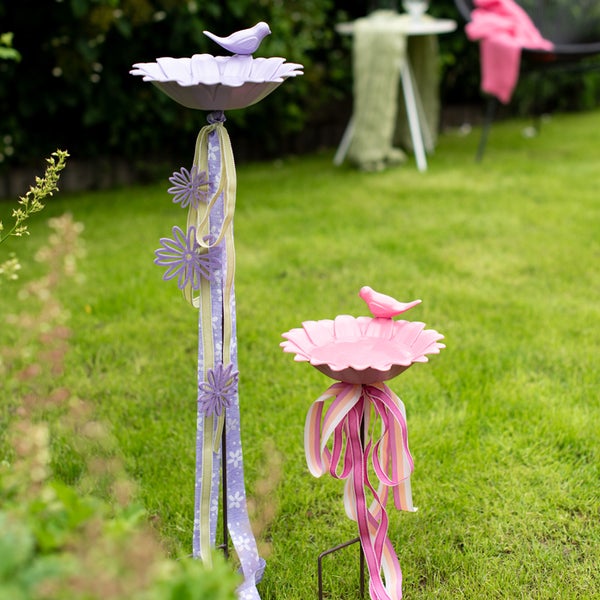 Zwei dekorative Vogeltränken mit Vogel-Figuren und Schleifen im Garten.