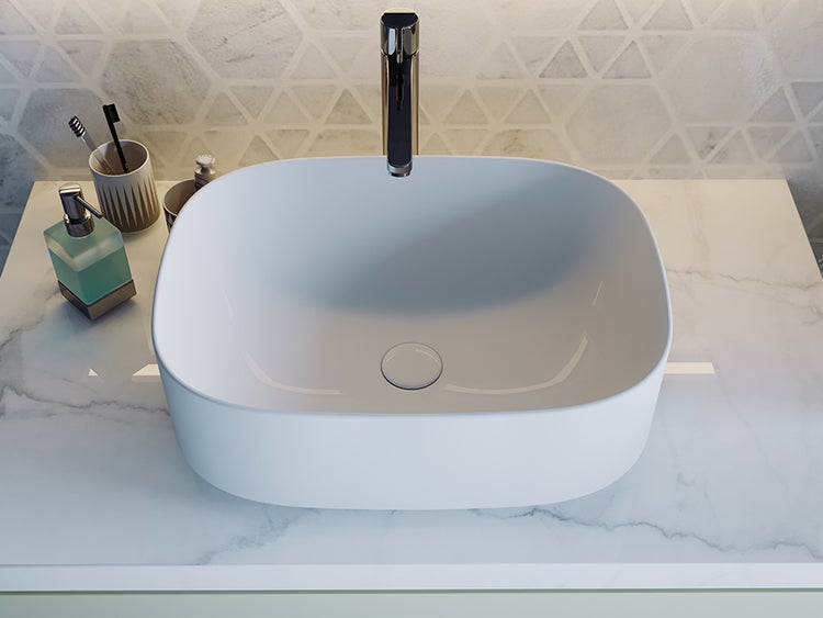 Modernes Aufsatzwaschbecken aus weißer Keramik in ovaler Form auf einer Arbeitsplatte in Marmoroptik mit verchromter Armatur.