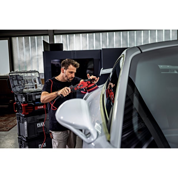 Ein Handwerker nutzt einen elektrischen Exzenterschleifer von Flex zum Polieren eines Autos in einer Werkstatt mit Flex Stapelboxen im Hintergrund.