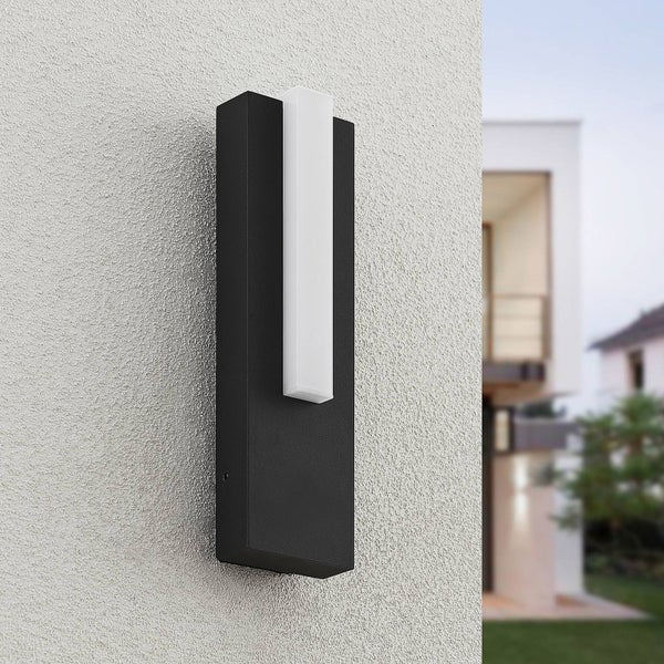 Moderne rechteckige Außenwandleuchte in Schwarz mit weißem Lichtelement, vertikal montiert an einer strukturierten Fassade eines Wohnhauses.