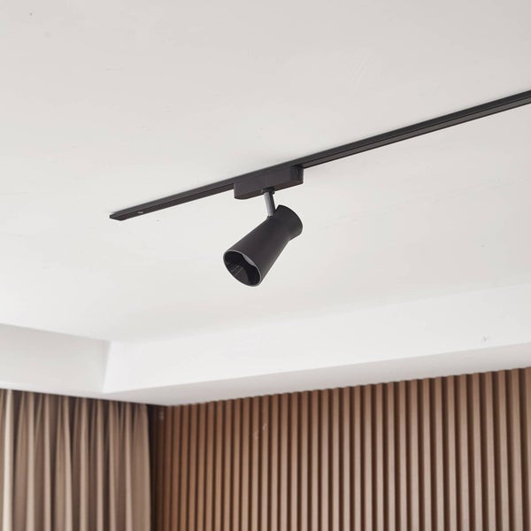 Schwarzer Strahler an einem Schienensystem an einer weißen Decke vor einer Wand mit Holzlamellen.