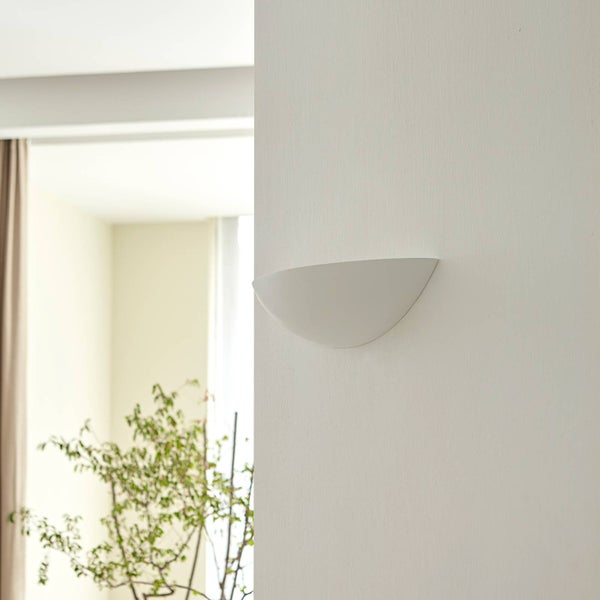 Weiße, halbkreisförmige Wandleuchte an einer weißen Wand in einem hellen Innenraum mit einer Pflanze im Hintergrund.