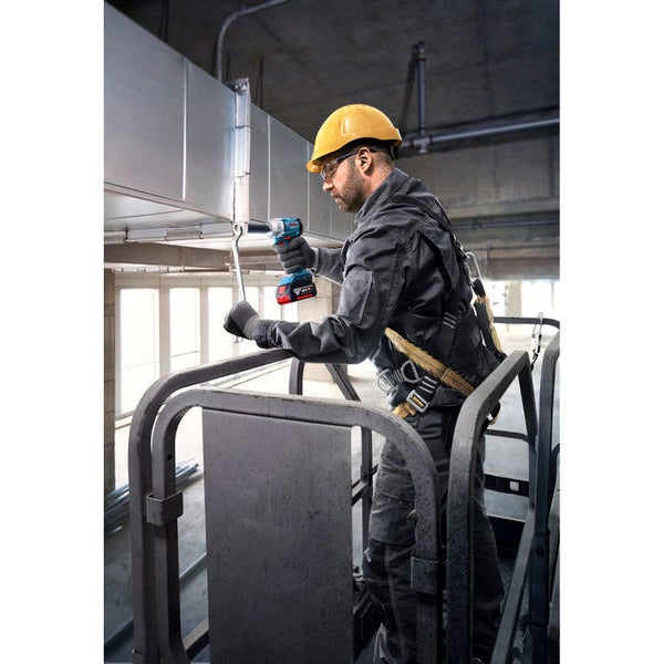 Ein Arbeiter mit Schutzhelm und Sicherheitsgurt montiert mit einem Akku-Schlagschrauber ein Lüftungsrohr.