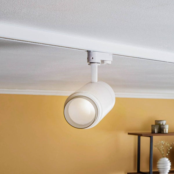 Weißer LED-Schienenstrahler an einer weißen Deckenschiene montiert, eingeschaltet in einem hellen, modern eingerichteten Raum.