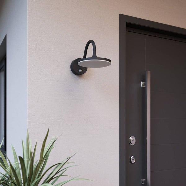 Moderne Außenwandleuchte mit Bewegungsmelder an einer Hauswand im organisierten Eingangsbereich neben einer Tür.