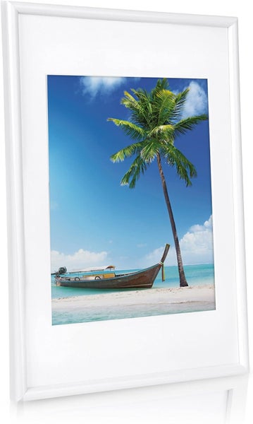 Ein gerahmtes Bild mit einem tropischen Strandmotiv, inklusive einer Palme und einem Holzboot vor blauem Himmel.