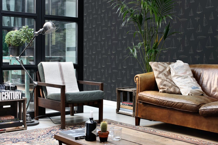 Helles Wohnzimmer im Industrial-Stil mit dunkler Tapete mit Segelboot-Muster, braunem Ledersofa, hölzernem Sessel und einer großen Zimmerpflanze.