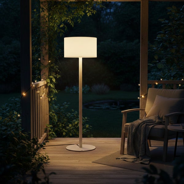 Moderne Stehleuchte auf einer Holzterrasse bei Dämmerung, daneben ein Holzsessel mit Kissen und Decke, umgeben von Pflanzen und Lichterketten.