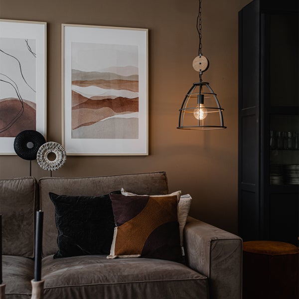 Wohnzimmer mit dunklem Sofa, dekorativen Kissen, abstrakten Wandbildern und einer hängenden Metalllampe mit einer Glühbirne.