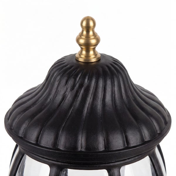 Detailansicht einer schwarzen Außenleuchte mit gerippter Haube und goldfarbener Zierspitze.