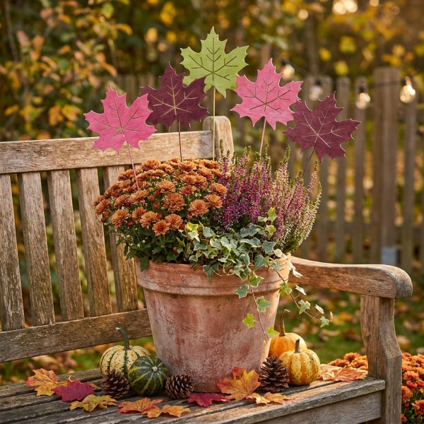 Herbstliche Blumendekoration im Tontopf mit Blättersteckern auf einer Gartenbank im Freien.