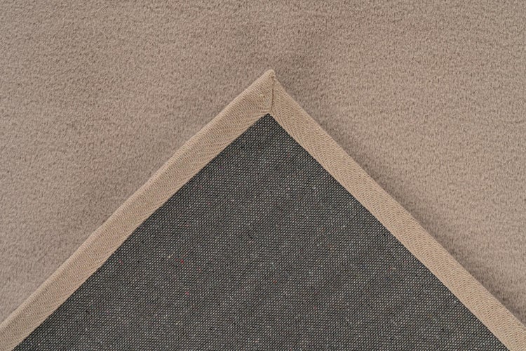 Nahaufnahme eines Teppichs mit weicher Textur, gewebter Einfassung am Rand und strukturierter Rückseite.