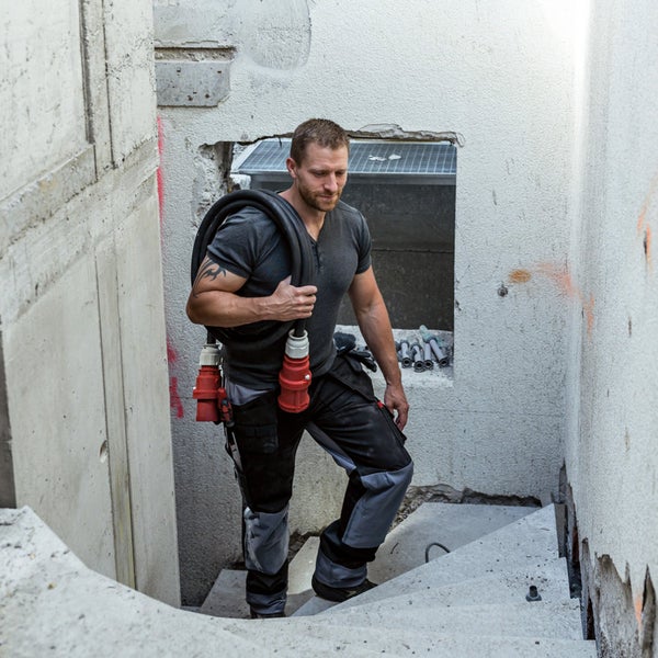 Ein Mann trägt ein Starkstromkabel die Treppe hinauf, Baustelle im Hintergrund
