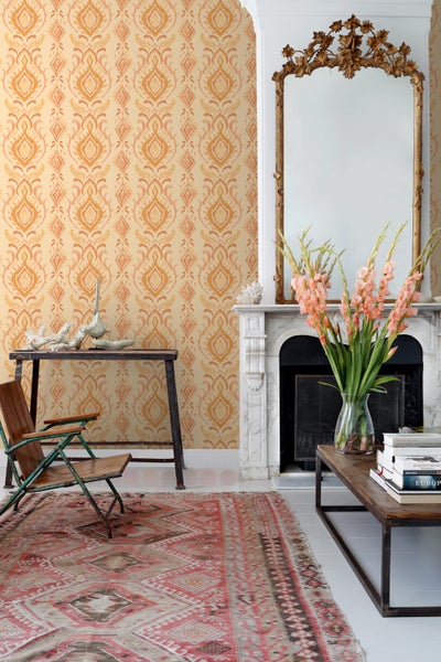 Wohnzimmer mit gemusterter Tapete, antikem Spiegel und Teppich