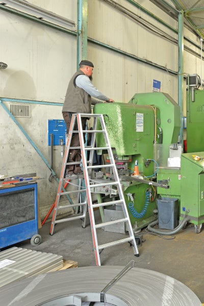 Mann auf einer Trittleiter vor einer Werkzeugmaschine in einer Werkstatt.