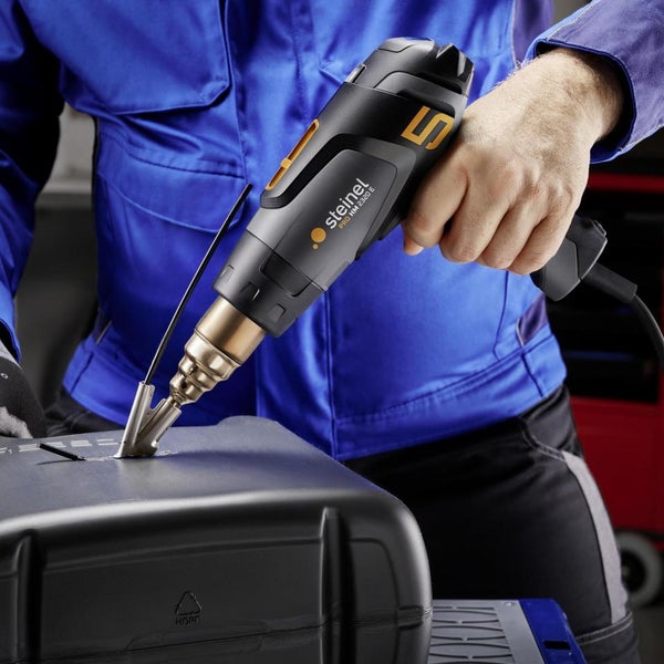 Steinel Professional Heißluftgebläse HG 2320 E beim Kunststoffschweißen an einem schwarzen Gehäuse mit Reduzierdüse und Schweißdraht.