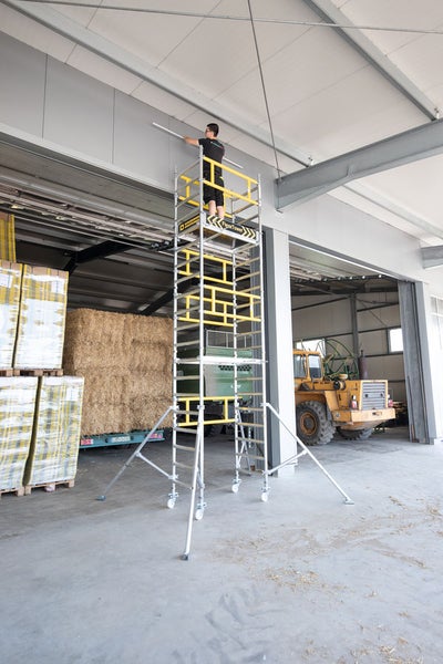 Person steht auf einem Gerüst in einer Lagerhalle und arbeitet.