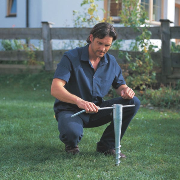 Ein Mann dreht eine verzinkte Einschraubhülse mit einer Eindrehstange in den Rasen im Garten.