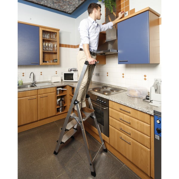 Mann steht auf einer Trittleiter in einer Küche.