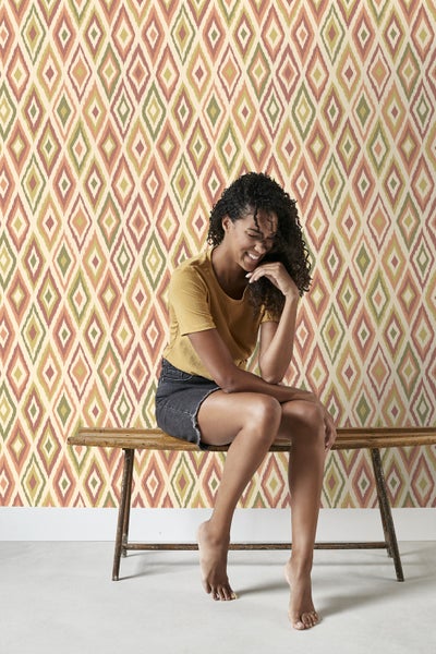 Frau sitzt vor einer Wand mit Rautenmuster-Tapete