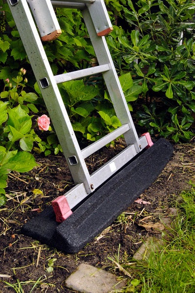 Aluminiumleiter mit schwarzer Sicherheitsmatte zur Stabilisierung auf weichem Boden im Garten.