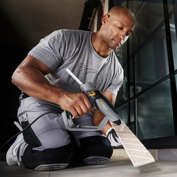 Handwerker trägt mit einer Steinel Heißklebepistole Kleber auf die Rückseite einer Fliese auf.