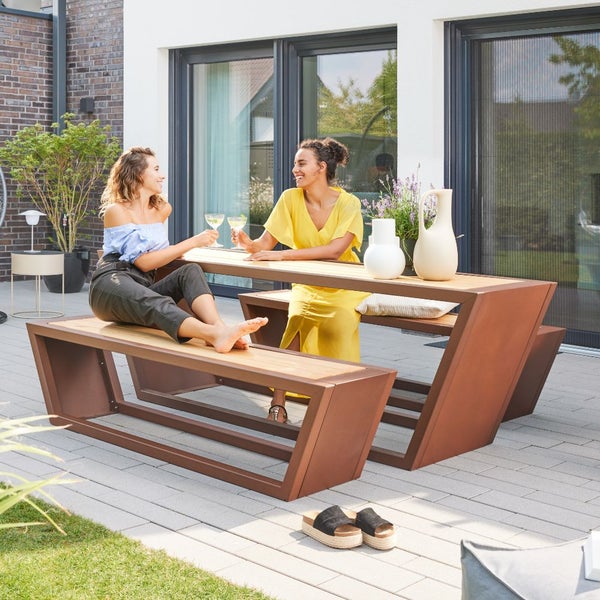 Modernes Gartenmöbel-Set bestehend aus Tisch und Bänken aus Metall und Holz auf einer gepflasterten Terrasse.