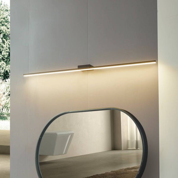 Moderne, lineare LED-Spiegelleuchte über einem ovalen Spiegel in einem hellen, organisierten Badezimmer.