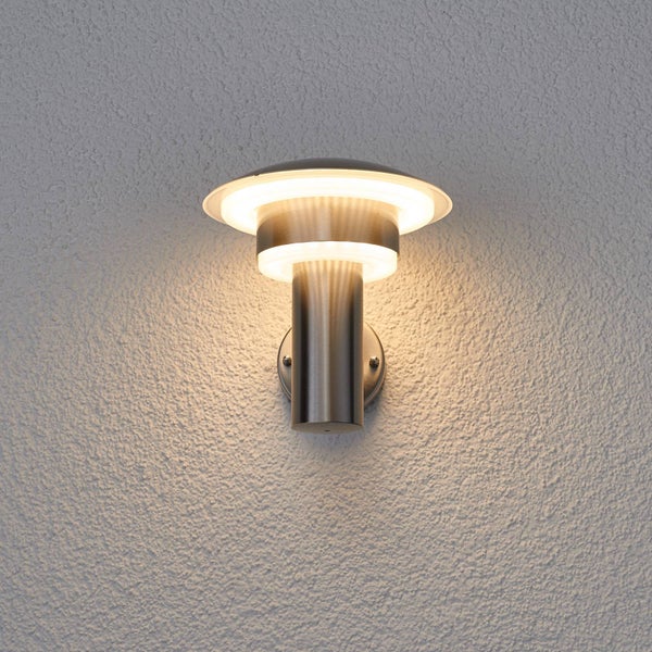 Moderne Außenwandleuchte aus Edelstahl mit warmweißem Licht an einer weißen strukturierten Wand.