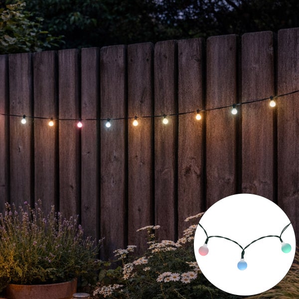 LED Lichterkette mit bunten Kugeln für die Dekoration im Garten, aufgehängt an einem Holzzaun mit Pflanzen im Vordergrund.