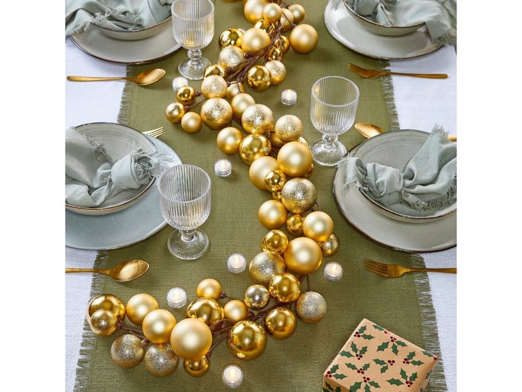 Festlicher Tischschmuck mit einer Girlande aus glänzenden und matten Kugeln als Weihnachtsdekoration auf einem gedeckten Tisch.