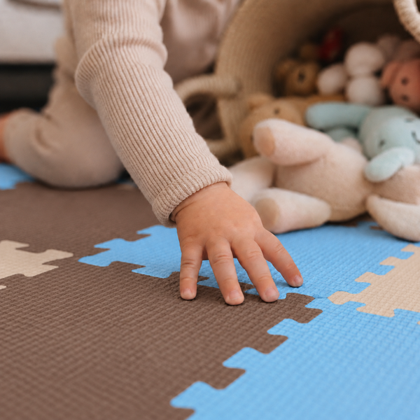 Kind spielt auf einer Puzzlematte aus Schaumstoff mit Kuscheltieren und Spielzeugkorb.