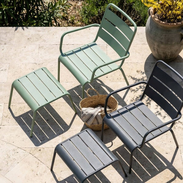 Moderne Gartenstühle aus Metall mit Armlehnen und passenden Hockern in Salbeigrün und Anthrazit auf einer hellen Steinterrasse.