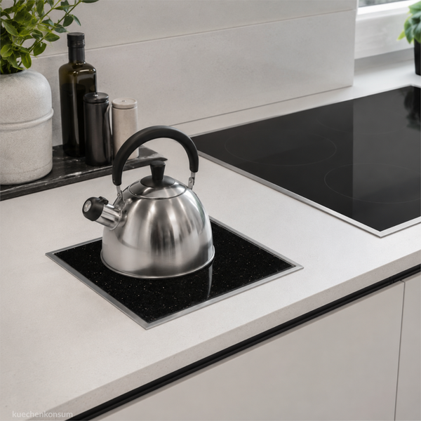 Edelstahlwasserkessel auf einem modernen Kochfeld in einer hellen, minimalistischen Küche mit weiteren Küchenutensilien auf der Arbeitsplatte.