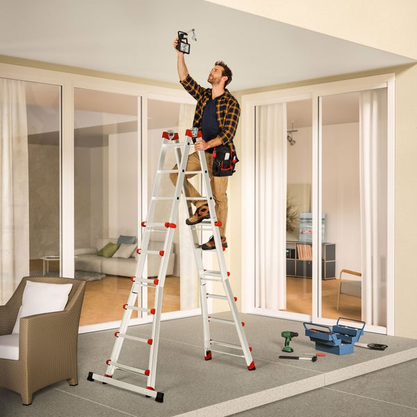 Mann auf einer Mehrzweckleiter, der eine Deckenleuchte inspiziert. Werkzeuge liegen bereit.