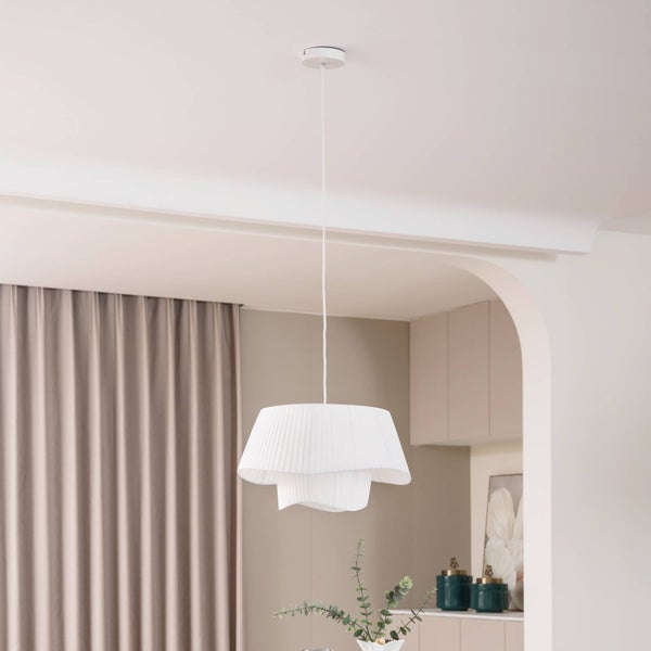 Moderne Pendelleuchte mit gestuftem, plissiertem Stoffschirm in einem hellen, minimalistischen Wohnraum mit Vorhängen.
