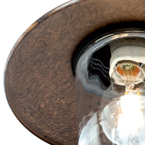 Nahaufnahme einer Außenleuchte mit texturiertem Metallschirm, klarem Glaszylinder und eingeschaltetem Leuchtmittel.