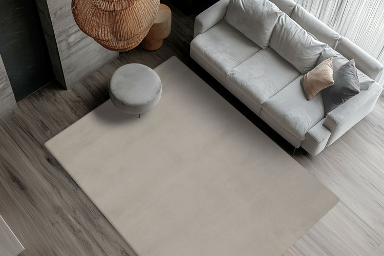 Ein moderner Wohnbereich in Draufsicht mit einem großen rechteckigen Teppich vor einem Sofa auf einem Holzboden.