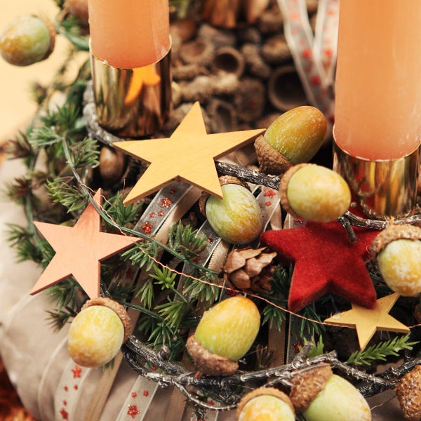 Weihnachtlicher Adventskranz mit Stumpenkerzen, Holzsternen, Eicheln und Tannenzweigen als Tischschmuck.