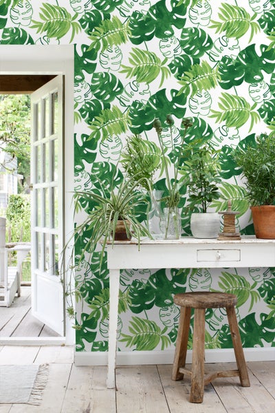 Raum mit weißer Tapete mit grünem Blätterdesign, weißem Tisch und Holzstuhl
