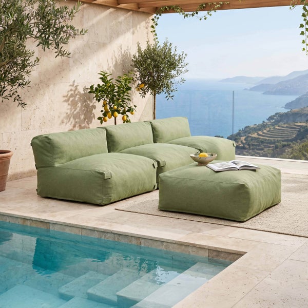 Modulares Gartensofa-Set in Grün auf einer hellen Steinterrasse neben einem Pool mit Blick auf das Meer und Olivenbäumen.