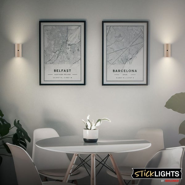 Wohnraum mit Tisch, Stühlen und Wandleuchten neben gerahmten Stadtplänen