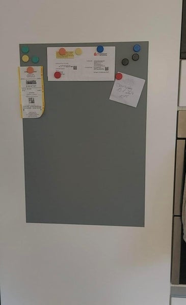 Rechteckige Magnetwand in Grau mit verschiedenen Notizen und runden bunten Magneten.