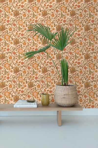 Wand mit floral gemusterter Tapete im Vintage-Stil, davor eine Holzbank mit Büchern, einem Krug und einer Zimmerpflanze in einem Korbtopf.