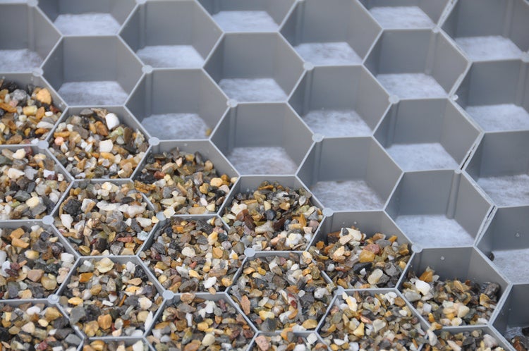 Kiesstabilisierungsgitter mit sechseckigen Waben, teilweise mit Kies gefüllt, mit integriertem Geotextilvlies.