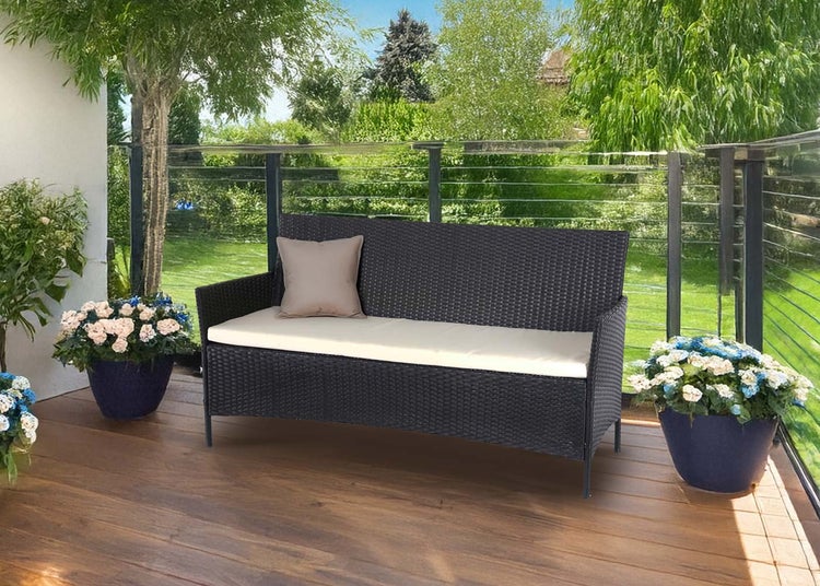 Moderne Gartenbank aus dunklem Polyrattan auf einer Holzterrasse mit Sitzkissen und Zierkissen in einer hellen Gartenumgebung.
