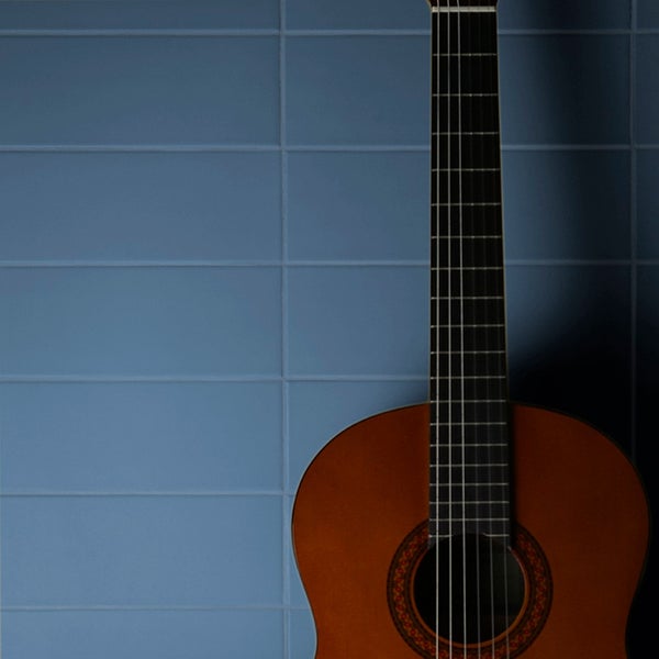 Eine akustische Gitarre steht vor einer Wand aus rechteckigen Wandfliesen im Riemchenformat.
