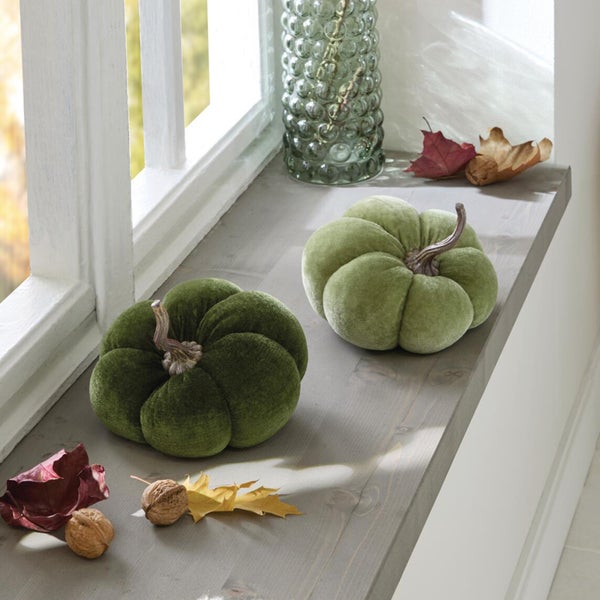 Zwei dekorative Kürbisse aus Samt in herbstlicher Fensterbankdekoration mit getrockneten Blättern und Walnüssen.