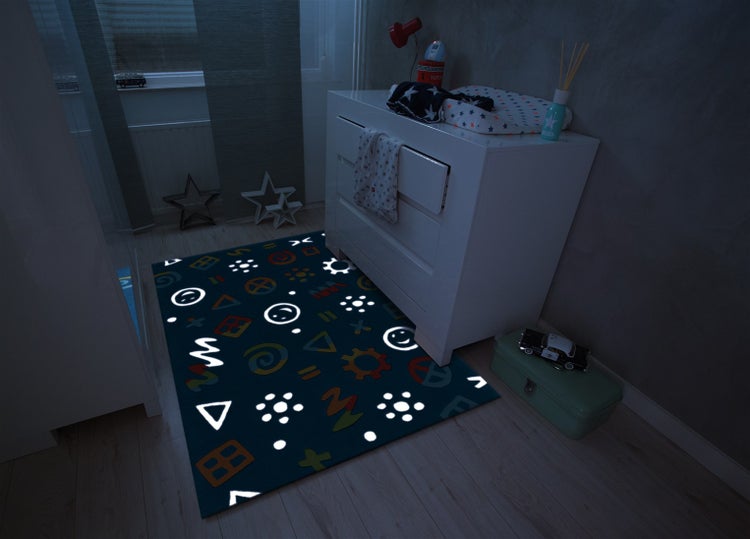 Kinderzimmer mit leuchtendem Teppich mit geometrischen Formen und Emoticons vor einer weißen Kommode in dunkler Atmosphäre.