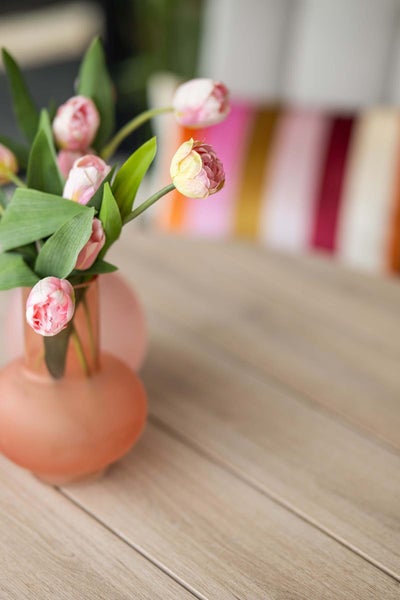 Künstliche Tulpen in einer matten Glasvase auf einer Holzoberfläche. Realistische Kunstblumen zur Dekoration.